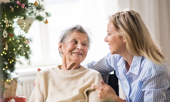 Junge Frau umarmt liebevoll ältere Frau, die sitzt.