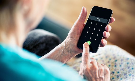 Eine alte Frau wählt auf einem Smartphone die Notrufnummer 112