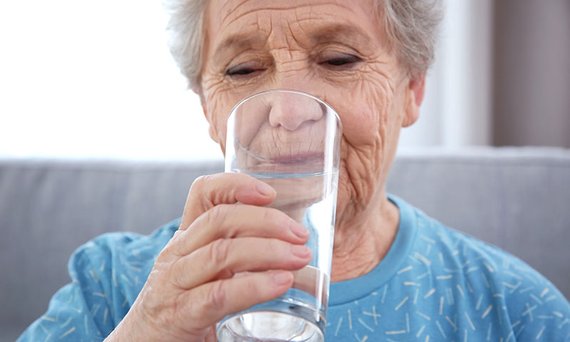 Eine Seniorin trinkt sitzend ein Glas Wasser.