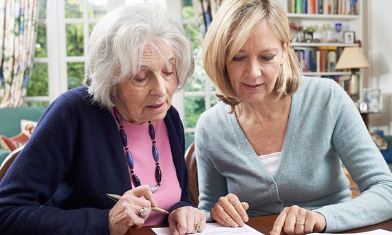 Eine alte und eine jüngere Frau sitzen über ein Dokument gebeugt am Tisch.