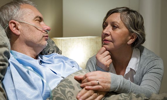 Eine Frau sitzt am Bett eines schwerstkranken Mannes