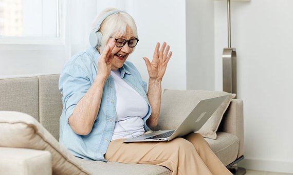Ältere Damit sitzt mit Laptop auf dem Sofa und führt einenen Videocall mit Angehörigen.