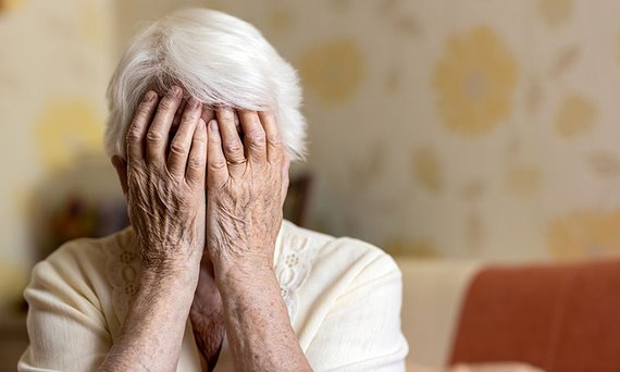 Eine alte Frau vergr&auml;bt ihr Gesicht in ihren H&auml;nden.